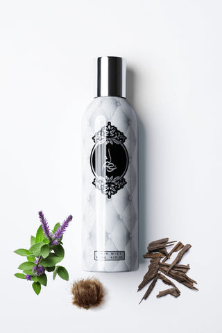 Marble-textured bottle with a black logo on a white background, surrounded by herbs and a feather byh Atyab Al Marshoud.